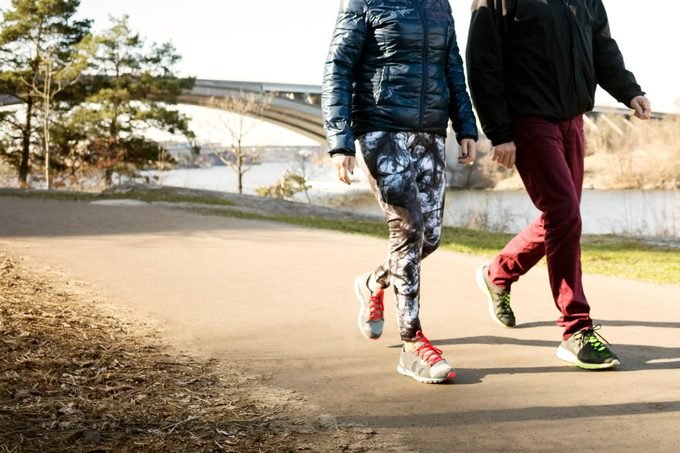 Section basse de l'homme et de la femme en tenue de sport marchant sur la route en automne